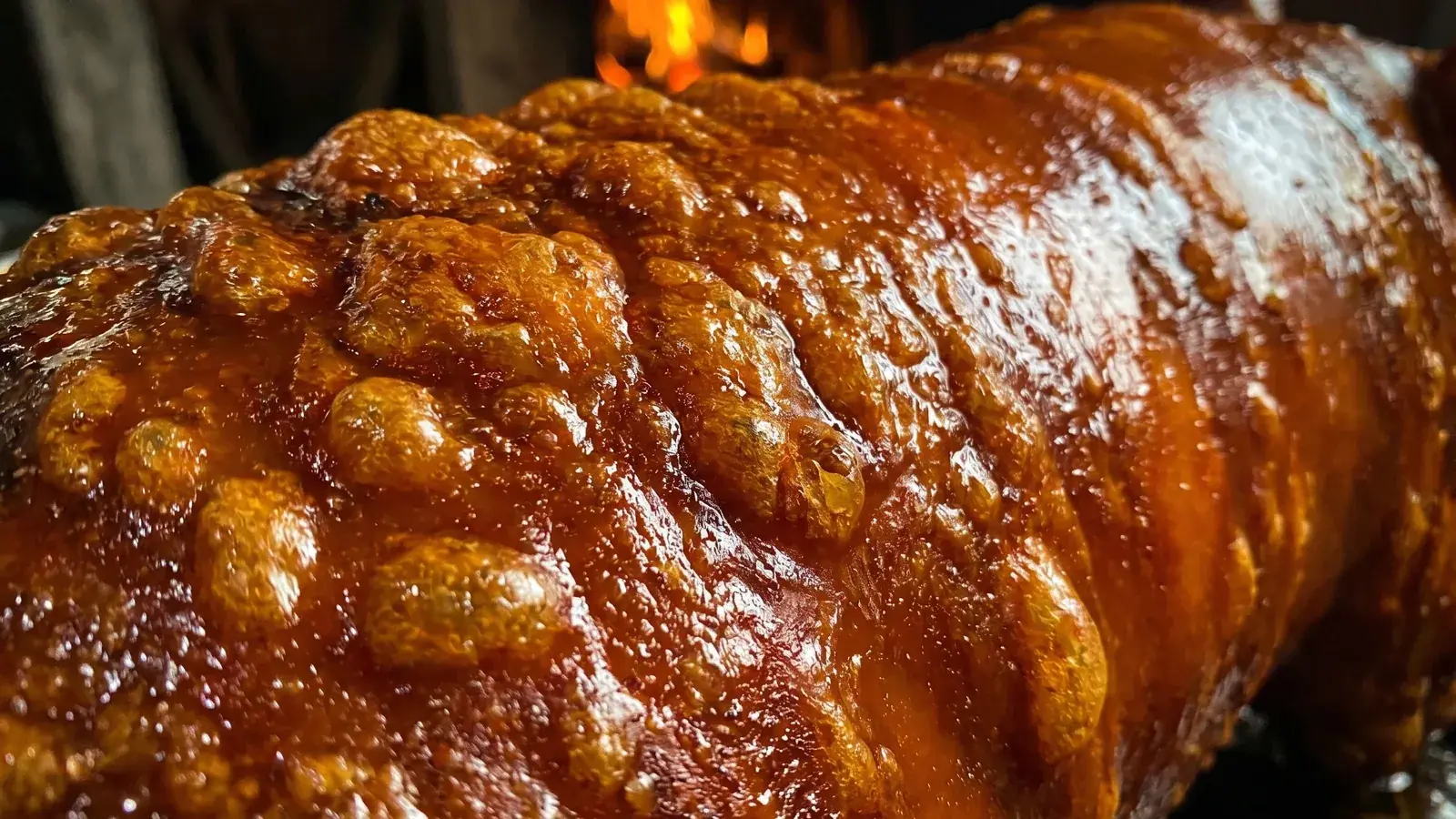 A whole Cebu lechon roasting, skin blistering, fire glowing behind